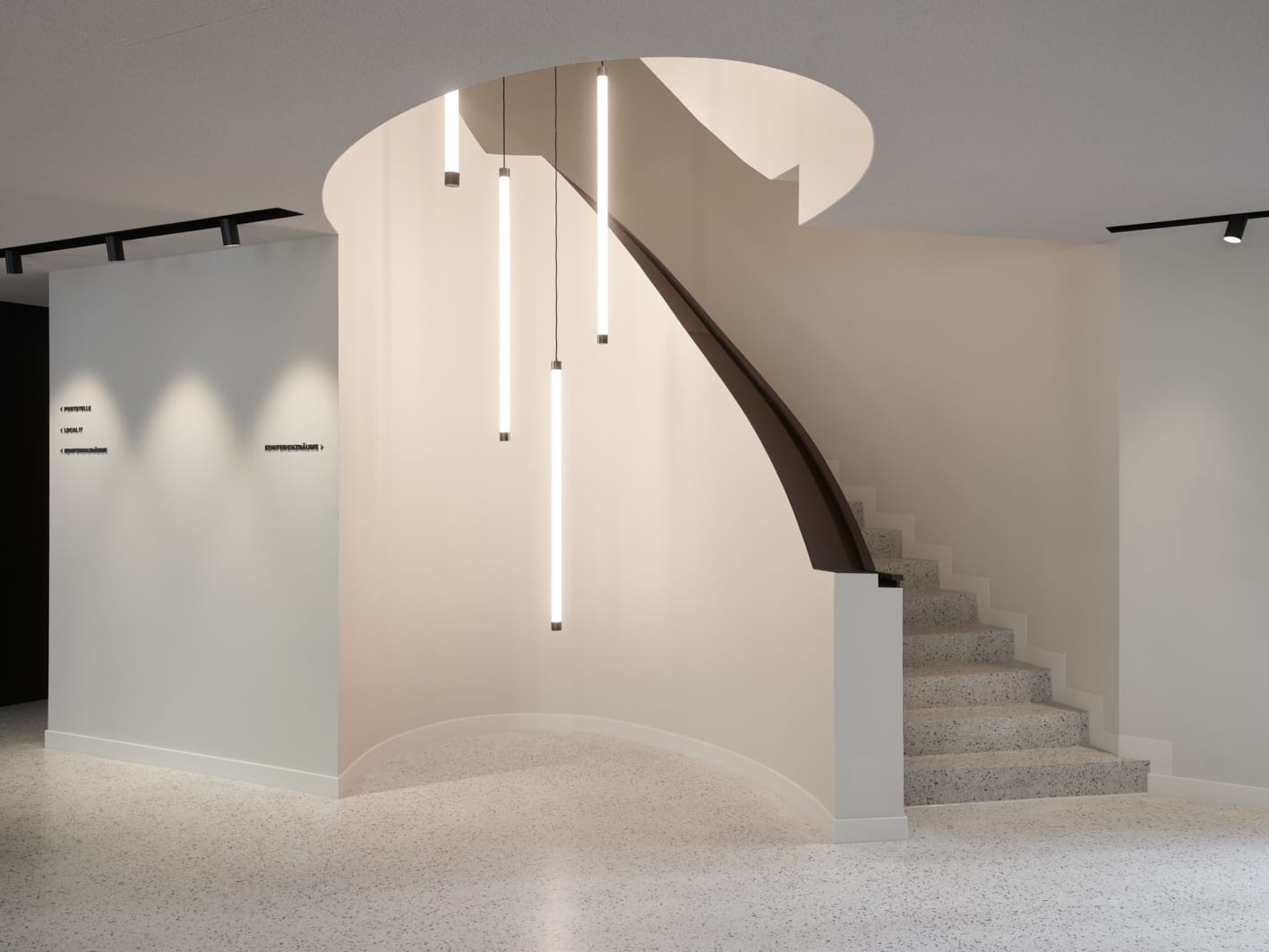 Moderne Wendeltreppe mit hängenden Lichtern im Raum.