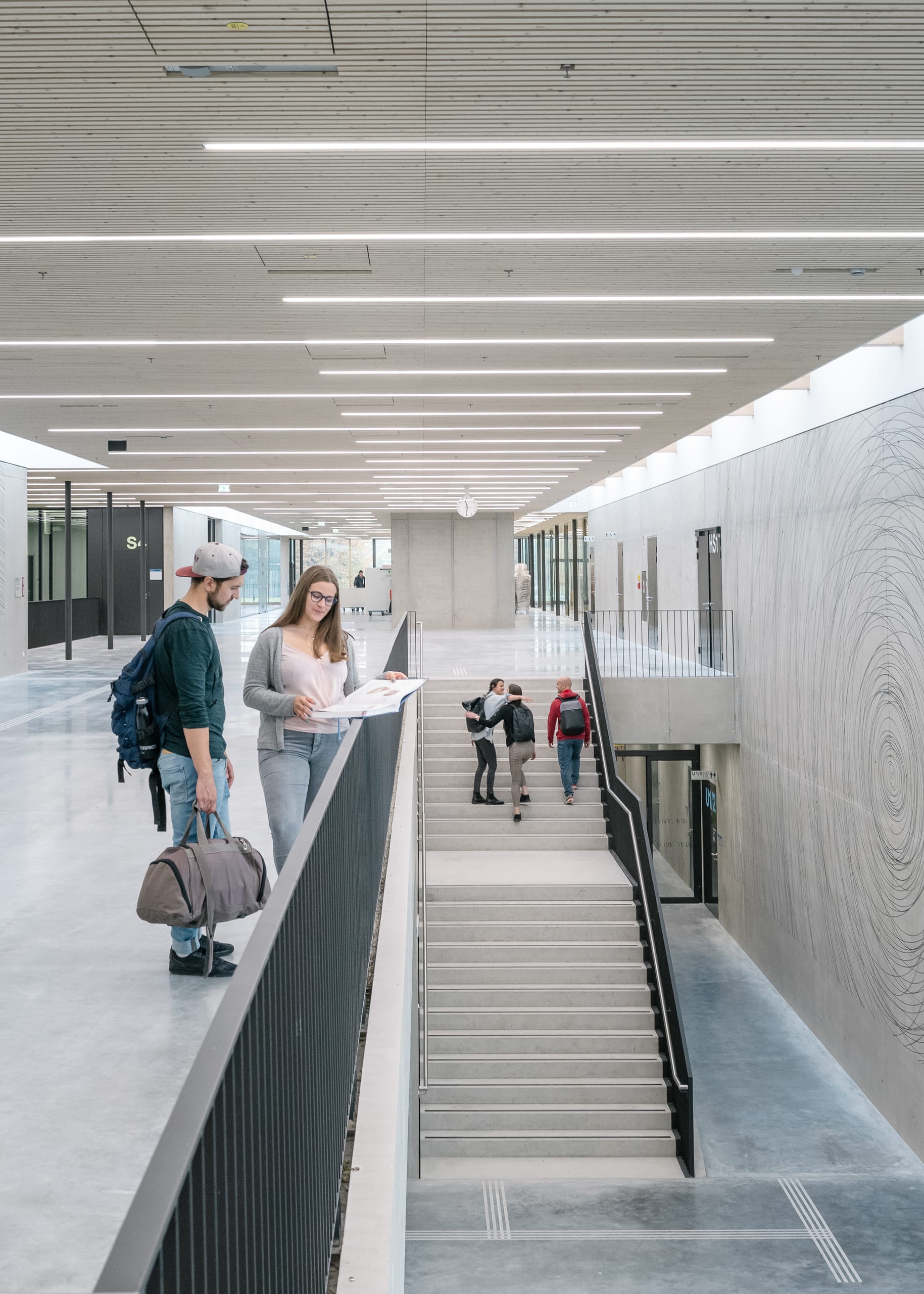 Studierende im modernen, hell beleuchtetem Gebäude mit Treppen.