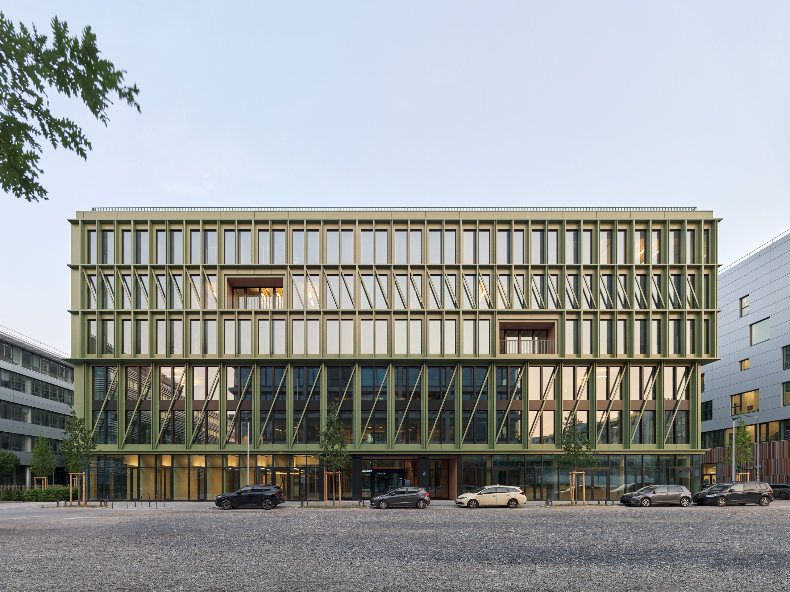 Modernes Bürogebäude mit Glasfassade, parkende Autos davor.